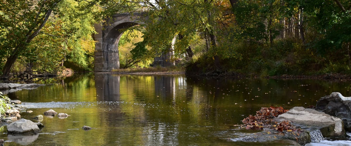 Eagle creek runs through a park in Indiana with an old, usused, arched bridge visible in the background