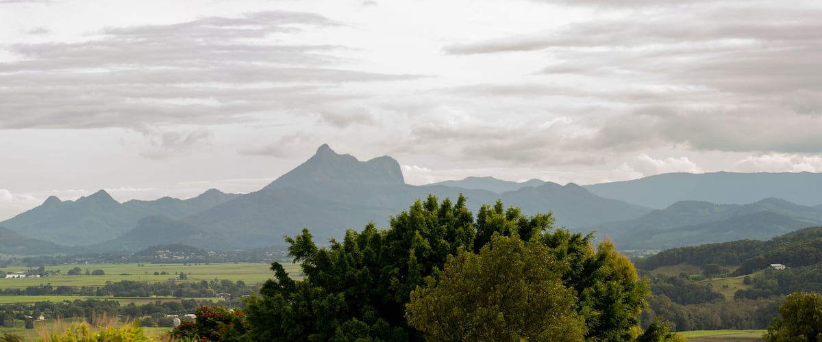 A mountainous landscape with a prominent peak, lush green fields, and scattered buildings.
