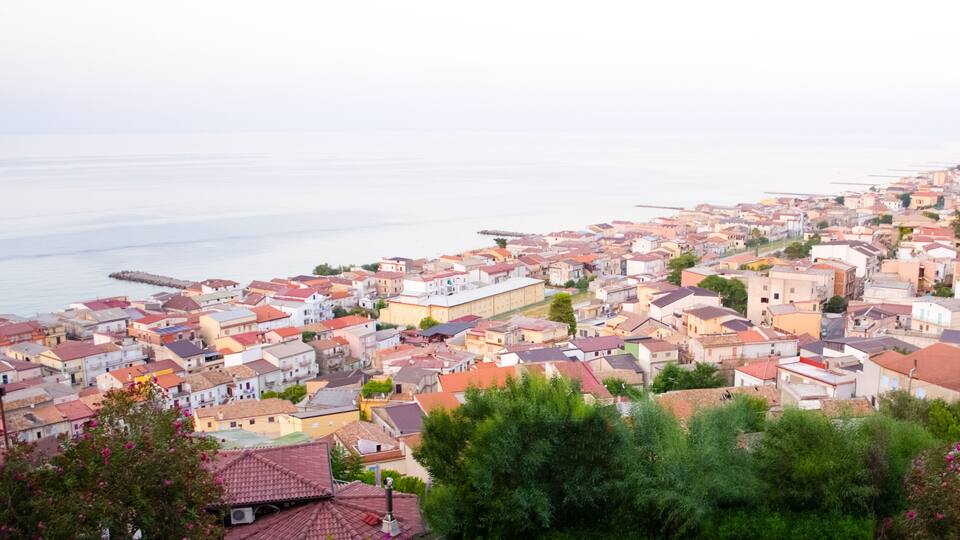 A coastal town with red-roofed buildings, a pier, and a view of the sea.