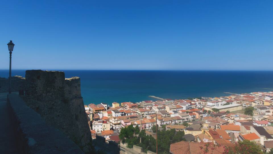 A coastal town with a prominent stone wall and a street lamp, overlooking the sea.