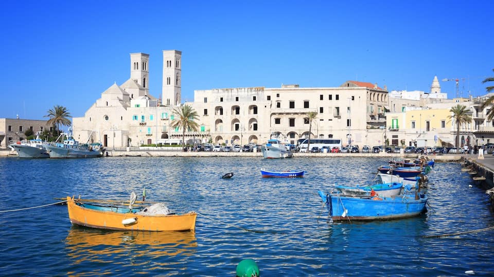 A harbor with several boats, a prominent building with two towers, and a clear blue sky.