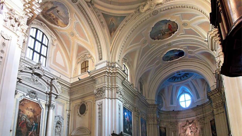 An ornate church interior with high ceilings, detailed frescoes, and a large altar.