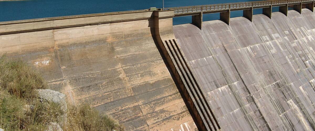 A dam with a bridge, a body of water, and a hilly landscape.