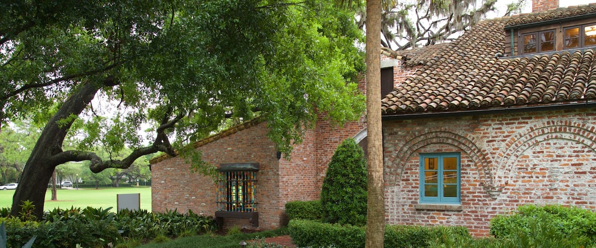 A brick house with a tiled roof, a curved brick pathway, and lush greenery.