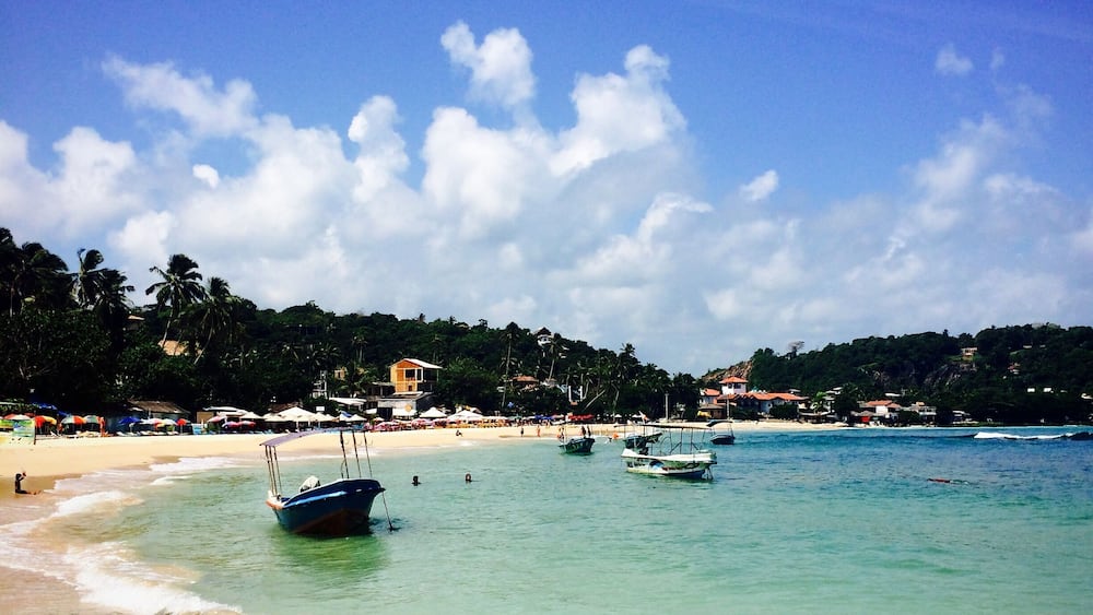 A beach with clear turquoise water, a sandy shore, and several boats anchored near the water's edge.