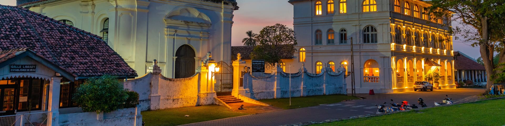 A historic building with ornate architecture and a well-maintained garden at dusk.