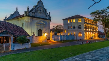 Un edificio histórico con arquitectura ornamentada y un jardín bien cuidado al anochecer.