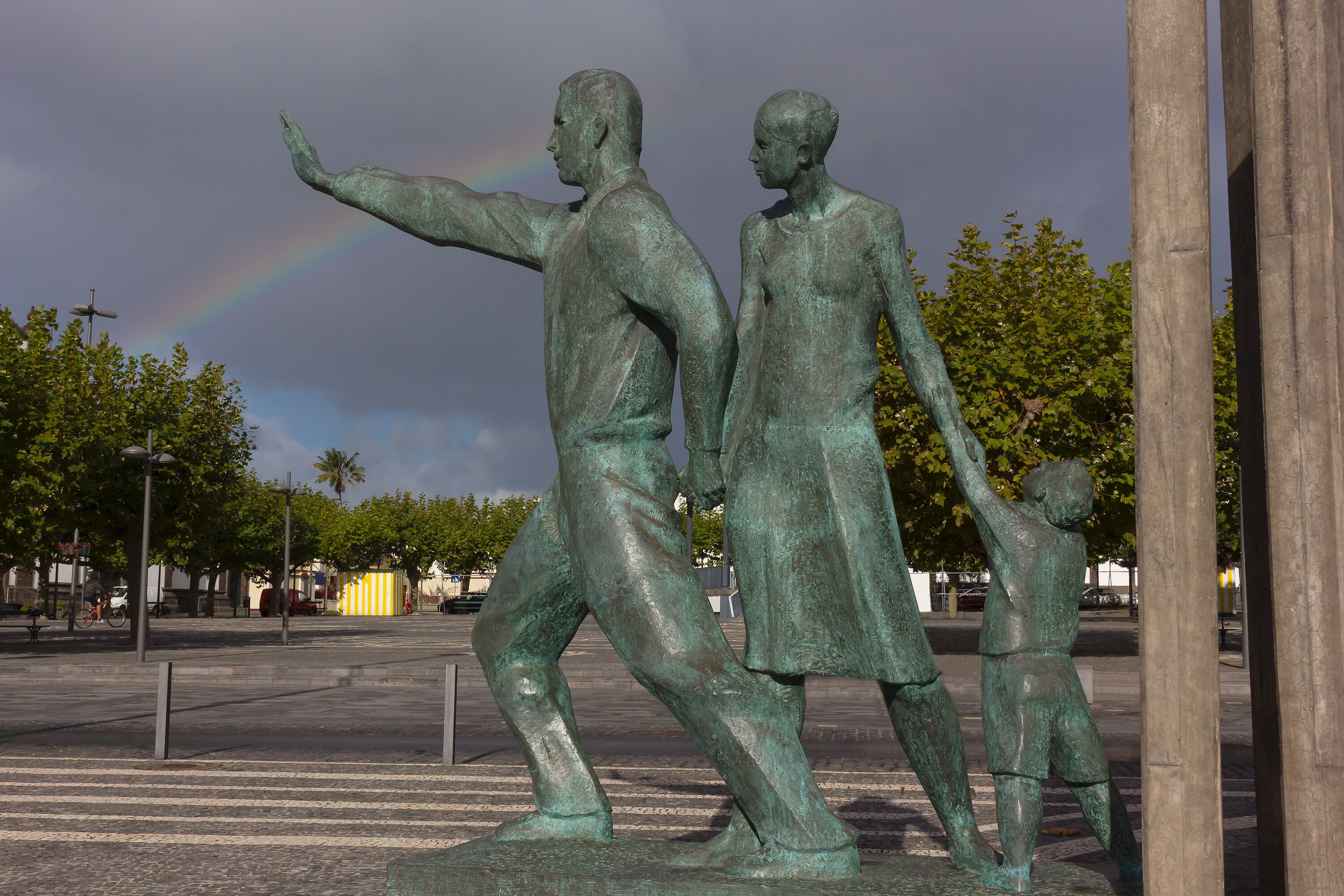 A bronze statue of a man and a child with a rainbow in the background.