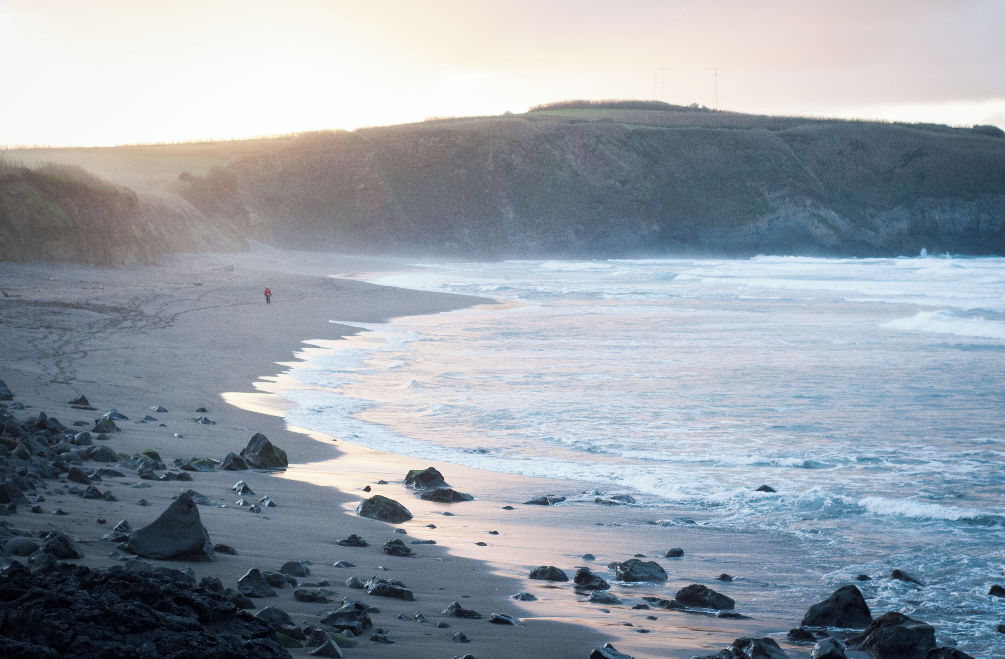 A rocky beach with waves crashing onto the shore and a person walking along the water's edge.