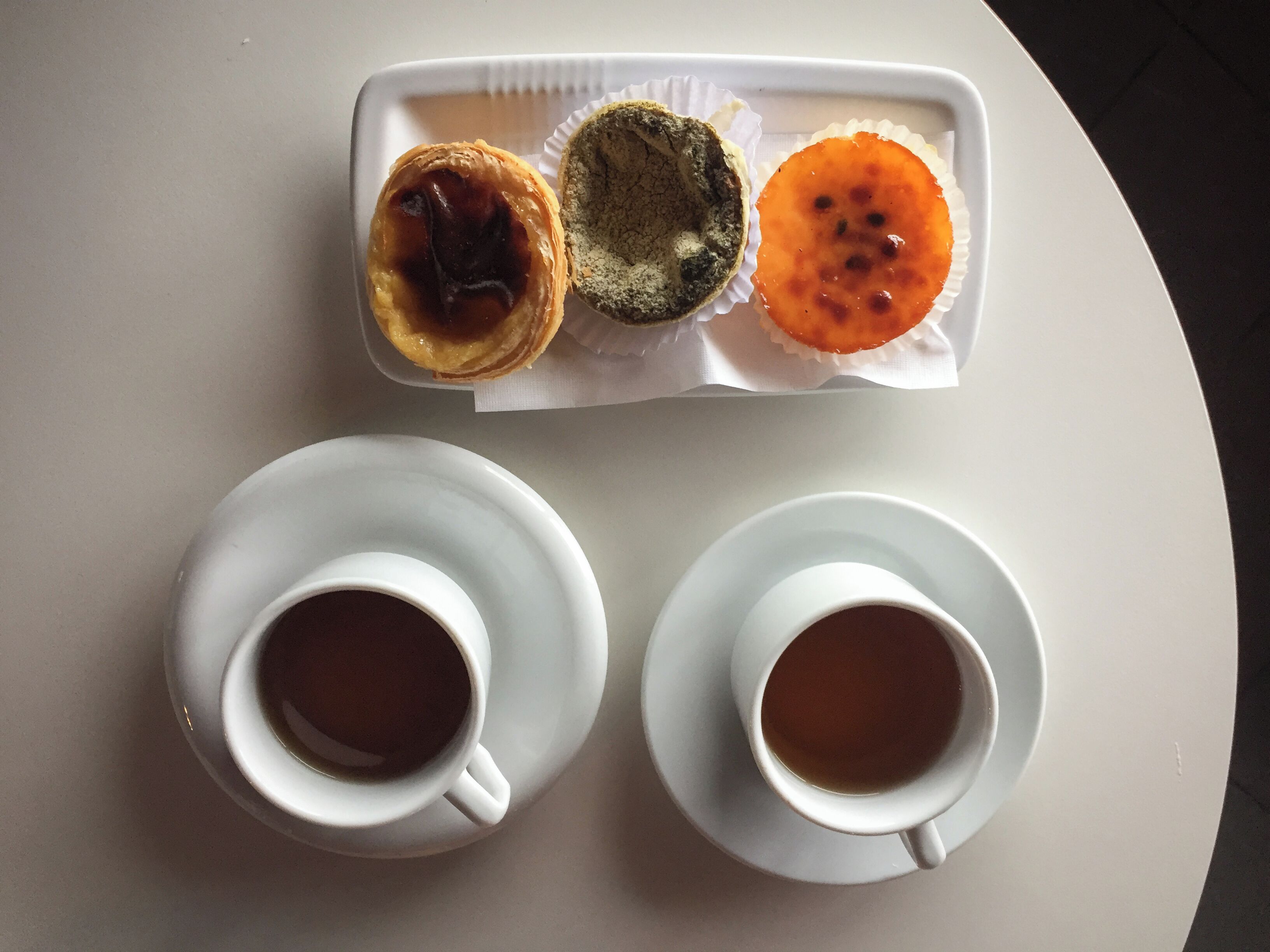A tray with three pastries and two cups of tea on a table.