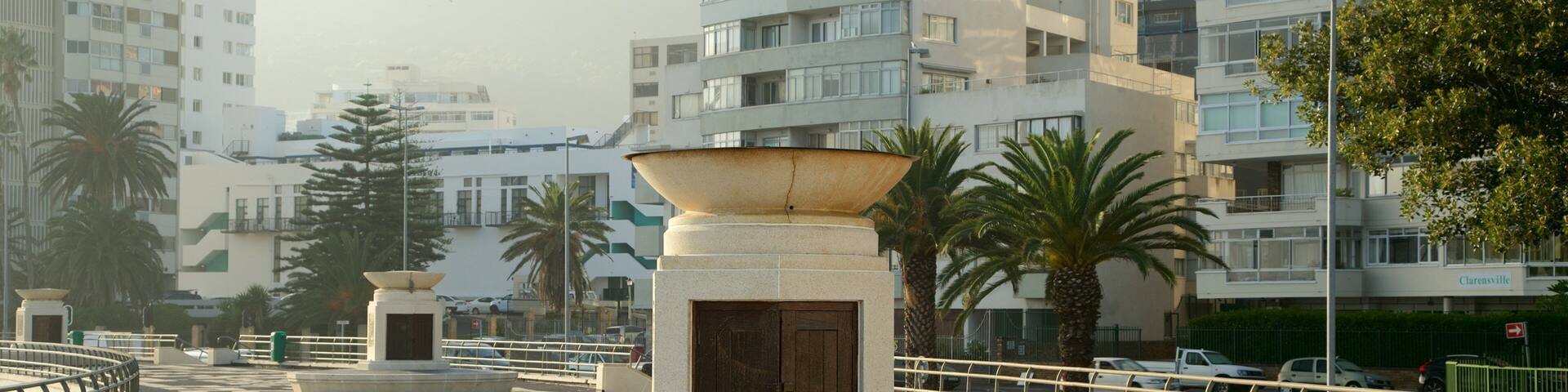 A roundabout with a central monument, palm trees, and modern apartment buildings in the background.