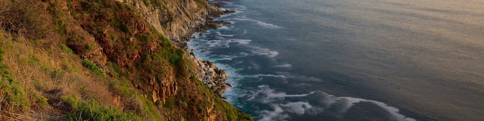 A coastal cliff with layered rock formations and a calm sea at sunset.