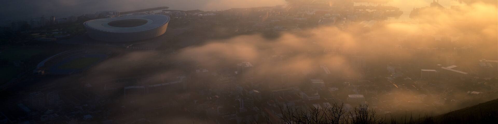 A cityscape with a large circular structure, likely a stadium, surrounded by fog and low-lying buildings.