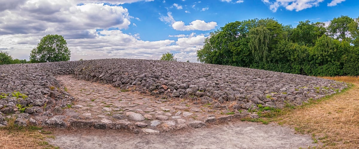 A stone circle with a central pathway, surrounded by trees and a partly cloudy sky.