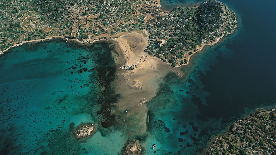 An aerial view of a coastal area with clear turquoise waters, sandy beaches, and rocky terrain.