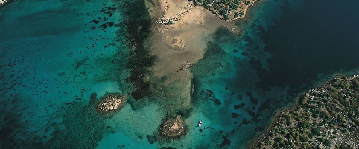 An aerial view of a coastal area with clear turquoise waters, sandy beaches, and rocky terrain.