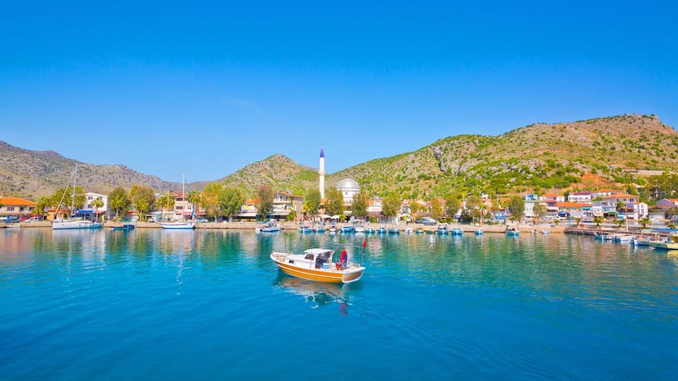 A coastal town with a clear blue sea, boats, and a prominent lighthouse.