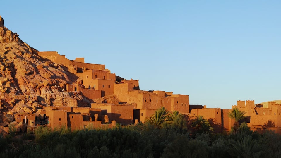 A desert landscape with a large, ancient stone structure on a hill, surrounded by traditional adobe buildings.