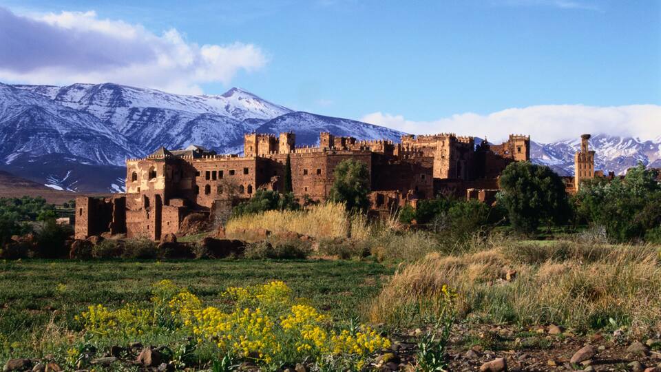 A historic castle with snow-capped mountains in the background.