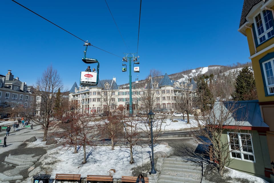 A ski lift with a sign, a snow-covered area, and buildings in the background.