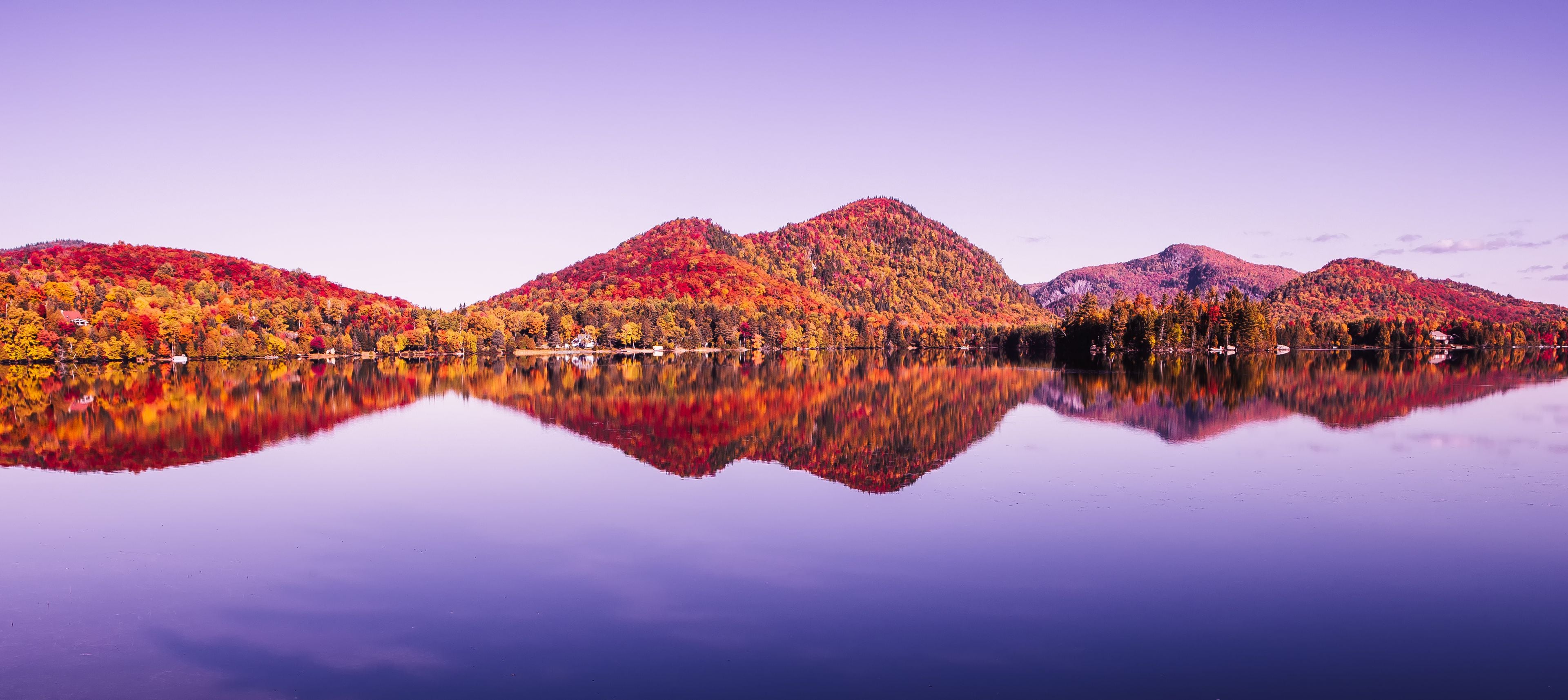 A lake reflecting colorful autumn trees and a small house on the shore.