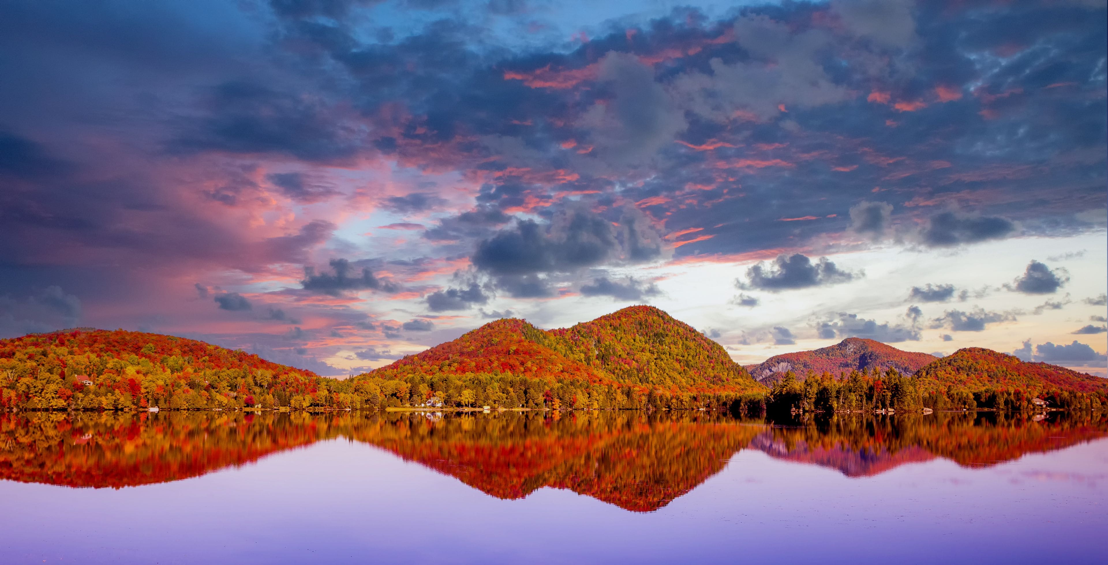 A lake reflecting colorful autumn foliage and a cloudy sky.
