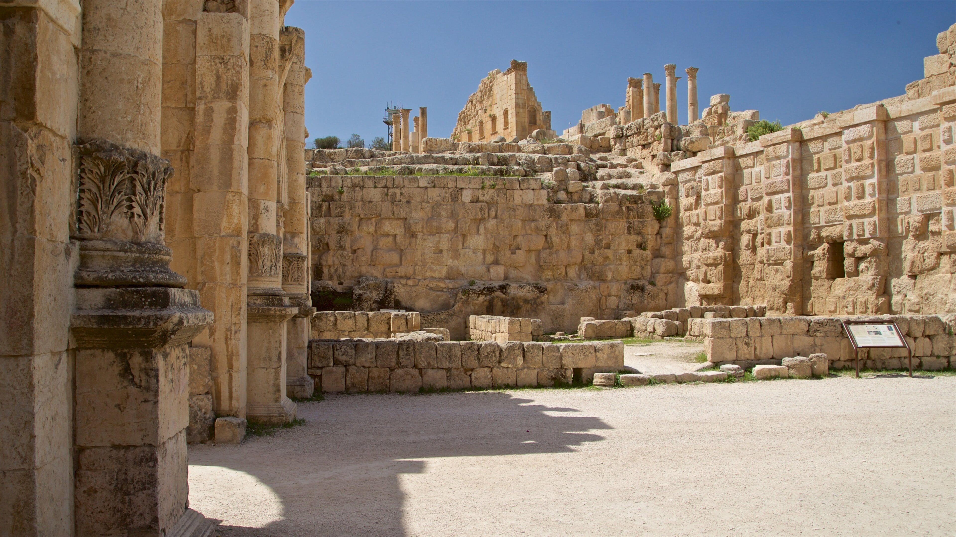 Ancient ruins with stone columns and a large stone wall.