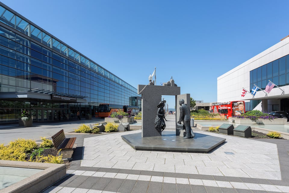 A modern plaza with a central sculpture, benches, and a glass building.