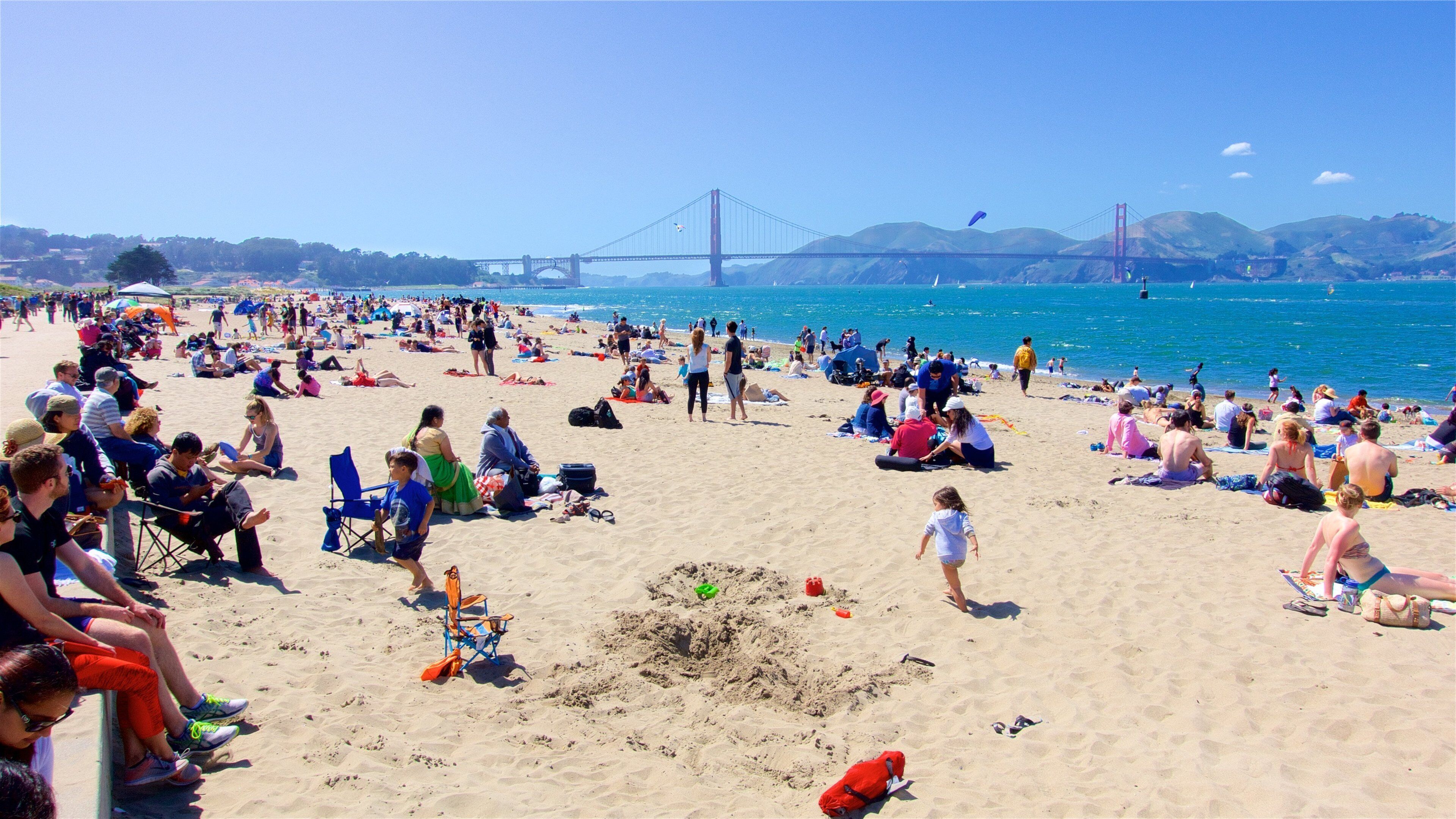 San Francisco showing a suspension bridge or treetop walkway and a sandy beach as well as a large group of people