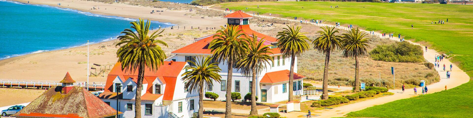 A coastal cityscape with a prominent dome-shaped building, palm trees, and a beach.