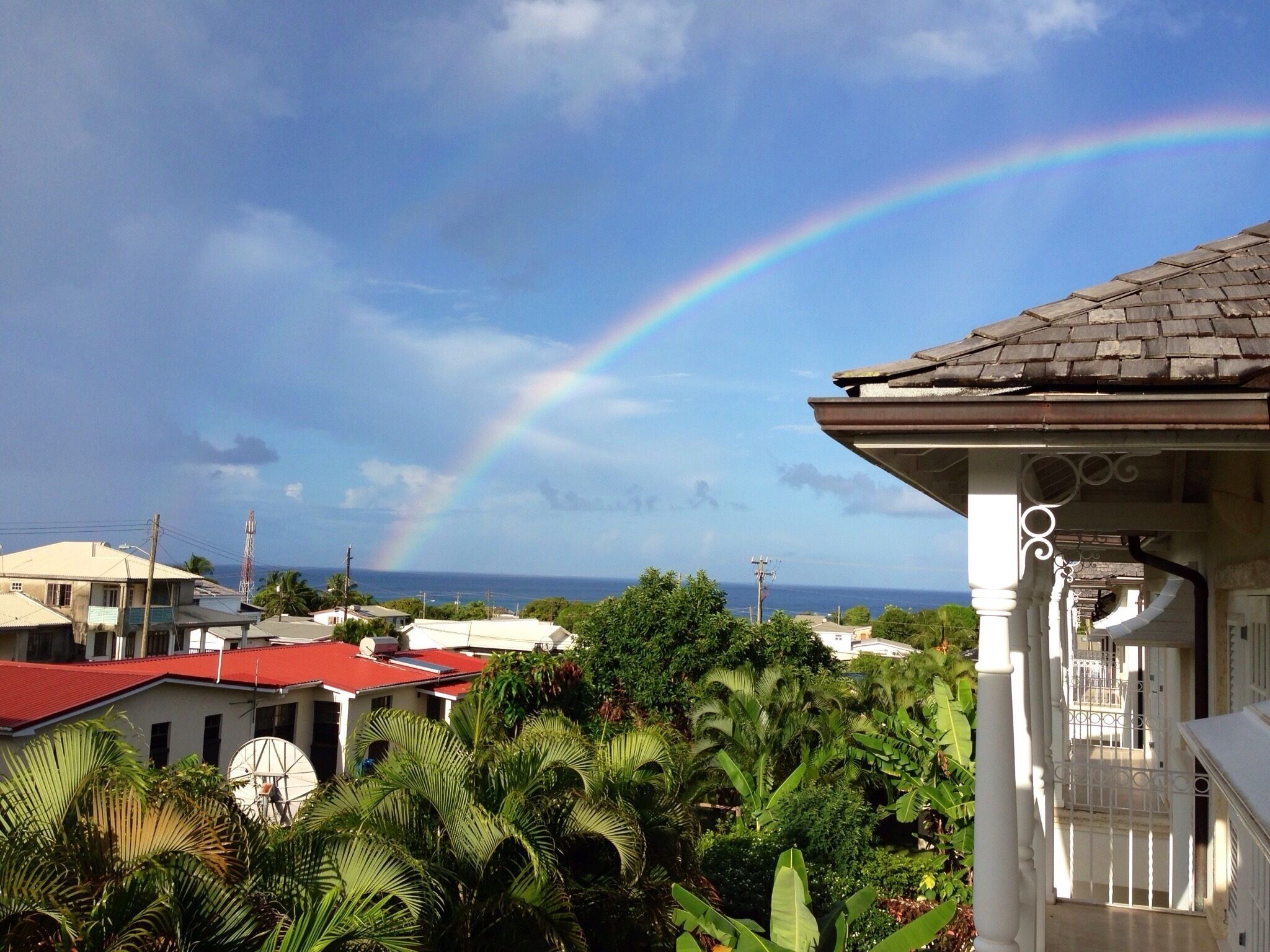 A house with a red roof, a white porch, and a view of the ocean with a rainbow.