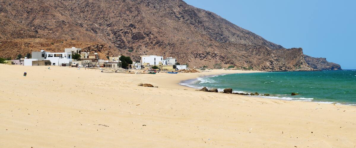 A sandy beach with buildings and a rocky mountain in the background.