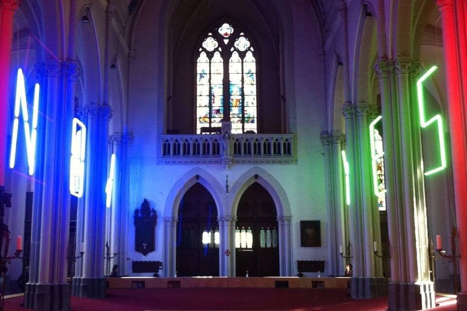 A cathedral interior with stained glass windows, arched doorways, and illuminated columns.