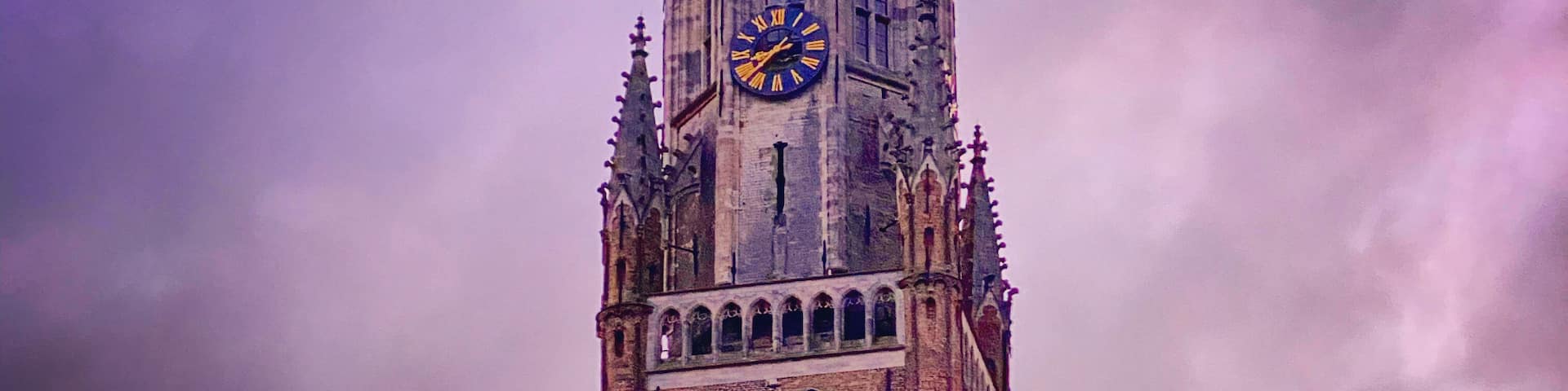 A historic tower with a clock, set against a dramatic sunset sky.