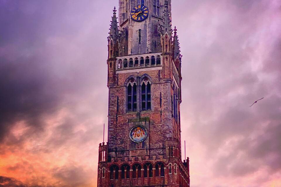Ein historischer Turm mit einer Uhr, vor einem dramatischen Sonnenuntergangshimmel.