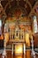 An ornate church interior with a detailed ceiling mural, a central altar, and stained glass windows.