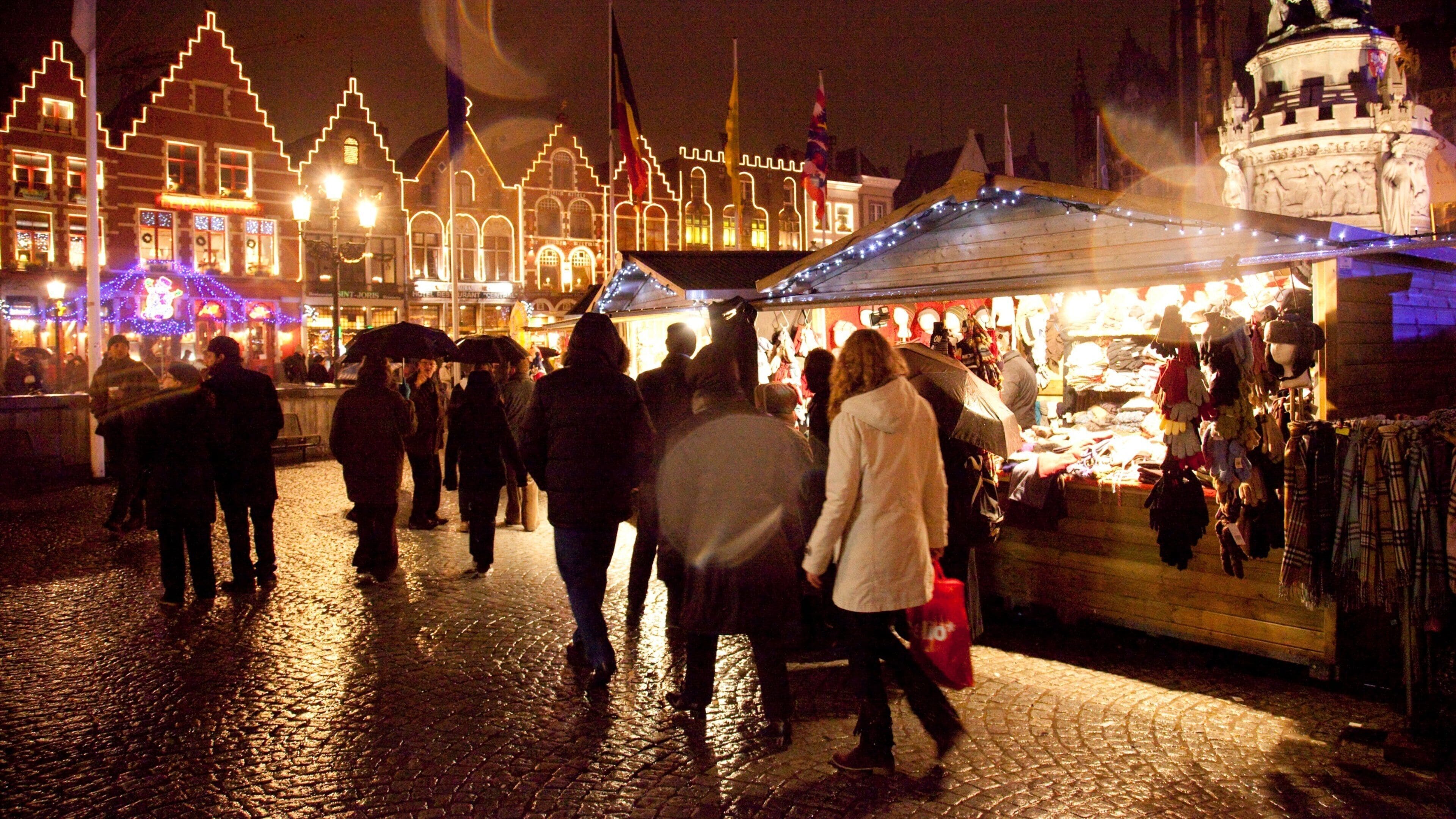 A nighttime market with people walking and shopping, illuminated buildings, and a prominent clock tower.