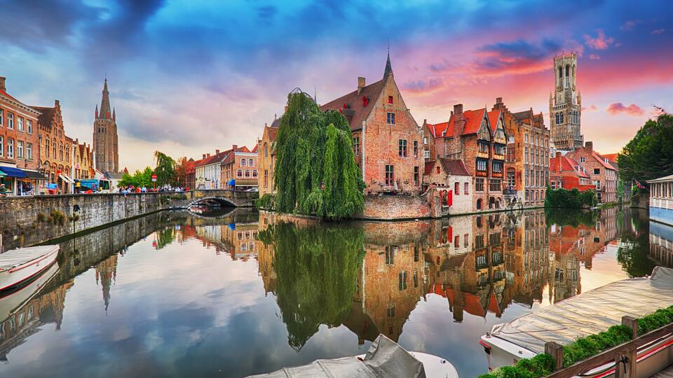 A canal with boats, a bridge, and historic buildings reflecting in the water.