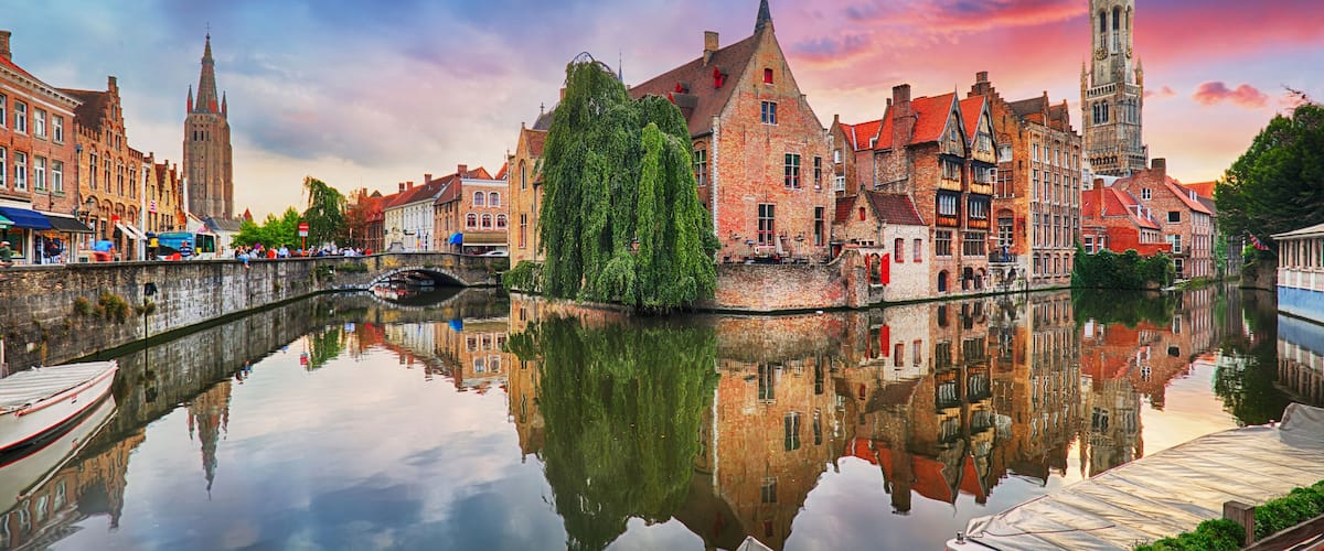A canal with boats, a bridge, and historic buildings reflecting in the water.