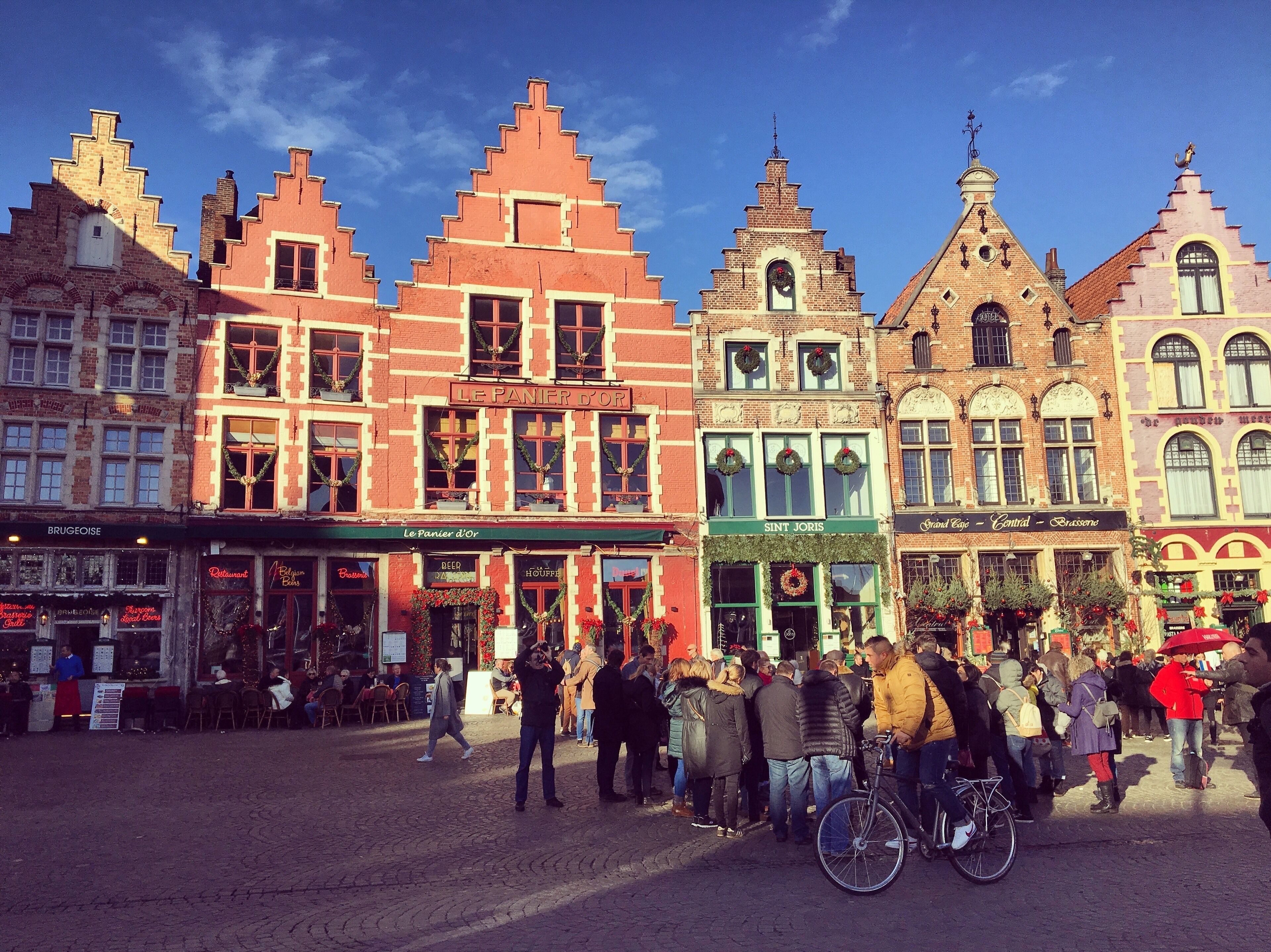 A bustling European market square with historic buildings, including a bakery and a restaurant.