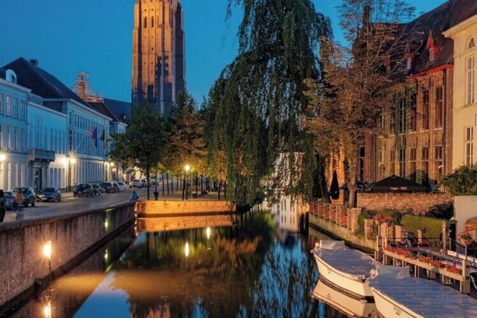 A canal with a boat docked on the right, a tall tower in the background, and buildings along the canal.