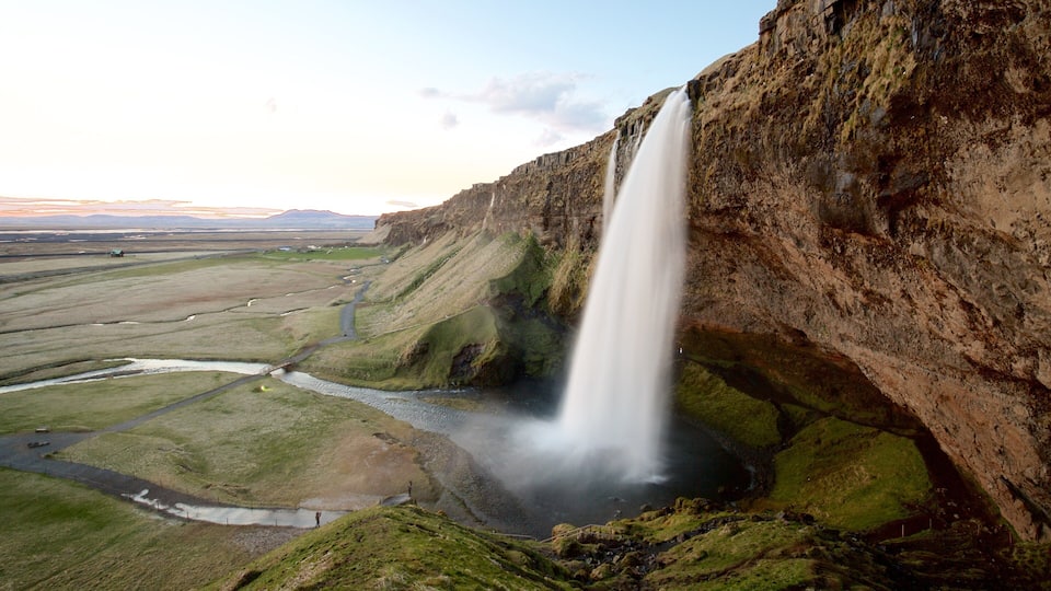 A waterfall cascading down a cliff into a valley with a river flowing through it.