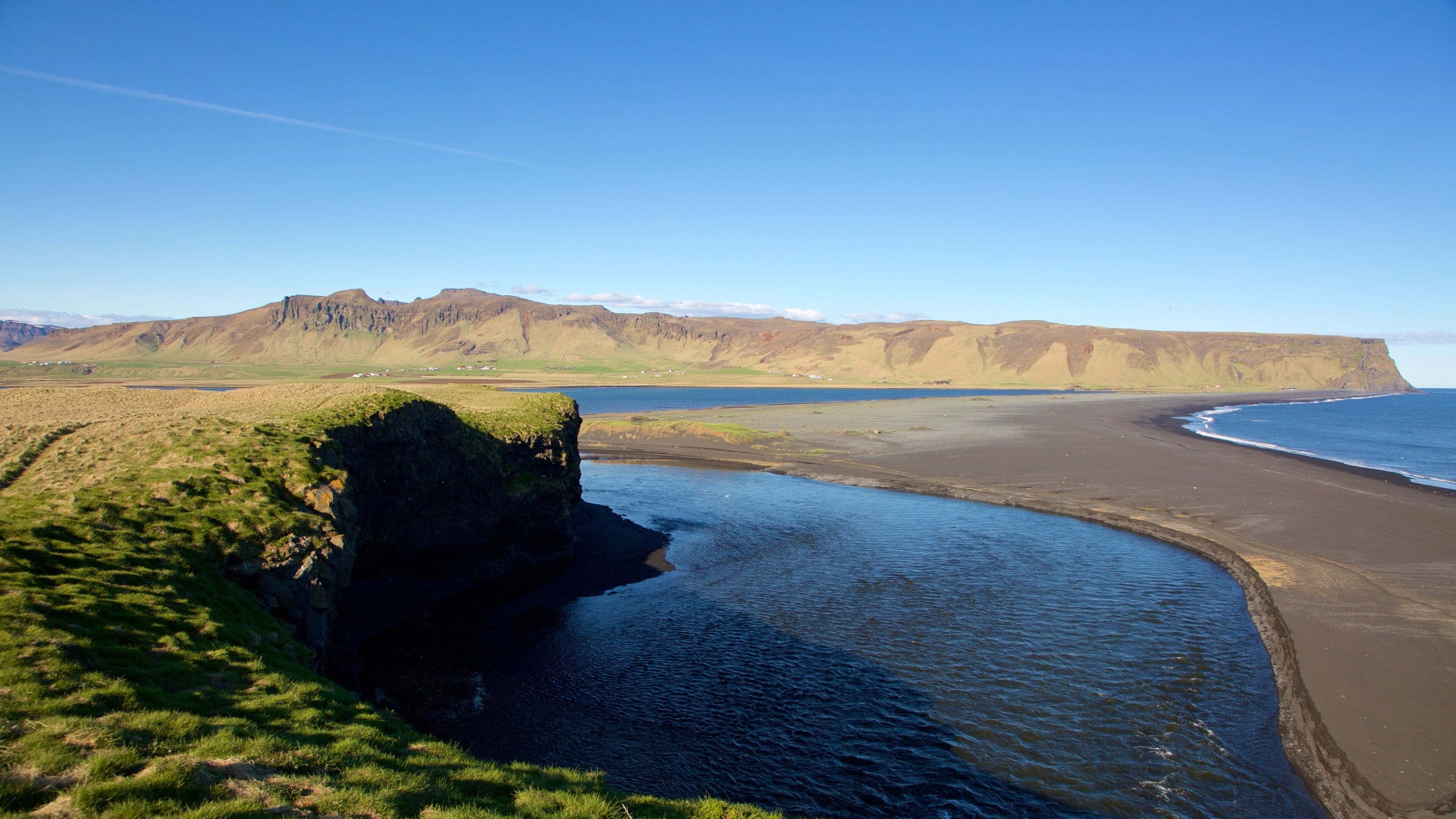 A coastal landscape with a cliff, beach, and distant mountains.