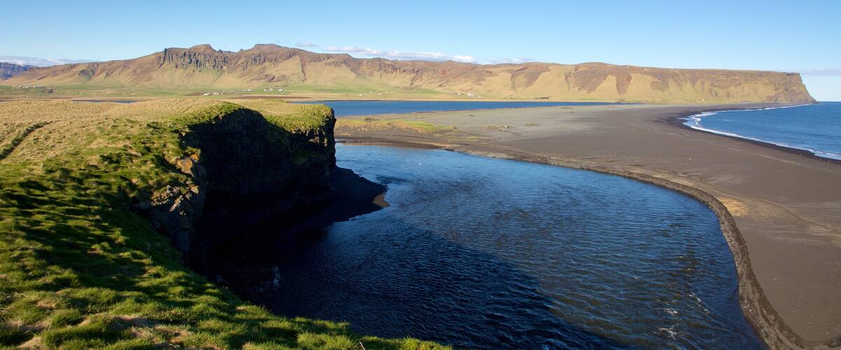 A coastal landscape with a cliff, beach, and distant mountains.