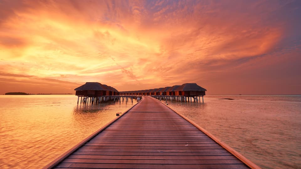 A wooden pier leading to overwater bungalows at sunset.