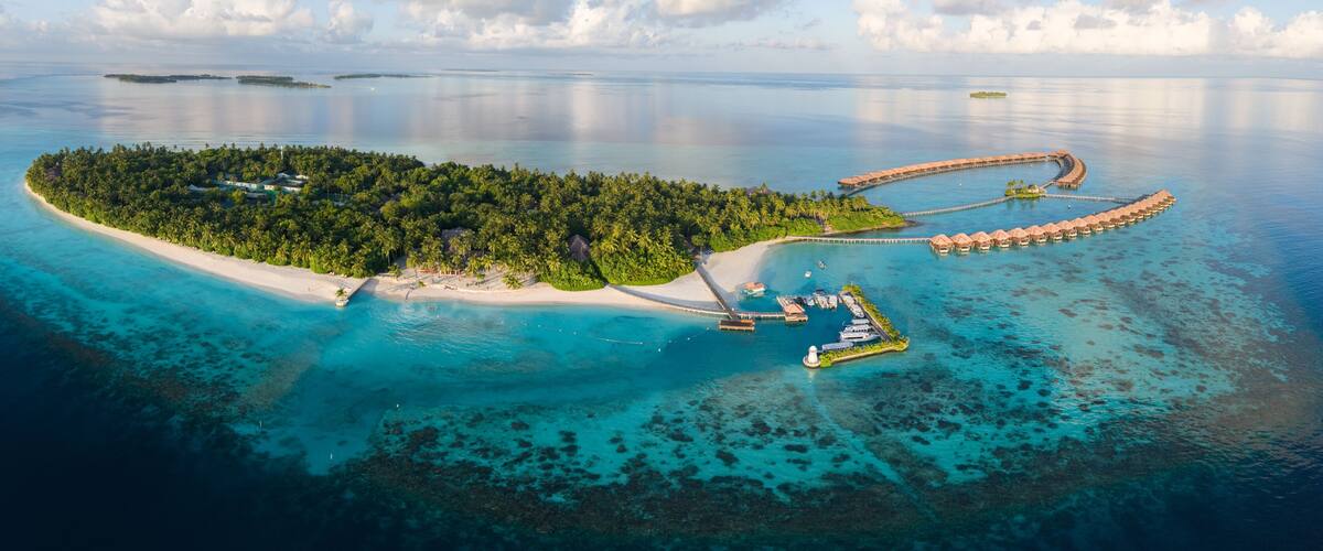 An aerial view of a tropical island with a beach, a lagoon, and overwater bungalows.