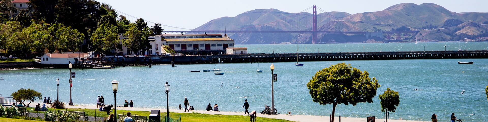 People laying in the grass in the park near the SF bay with the Golden Gate bridge in the background.
