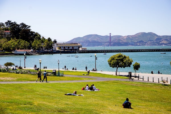 People laying in the grass in the park near the SF bay with the Golden Gate bridge in the background.