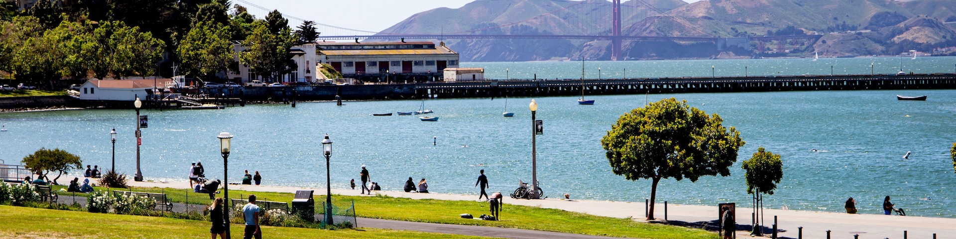 People laying in the grass in the park near the SF bay with the Golden Gate bridge in the background.