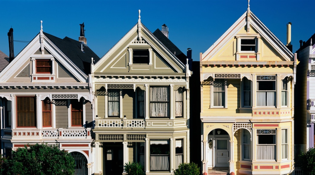 These are the historic Victorian homes on Steiner Street. They are all painted in pastel colors. They all have a pointed gable at the top of each house and a small balcony on the second floor. There is a blue sky.